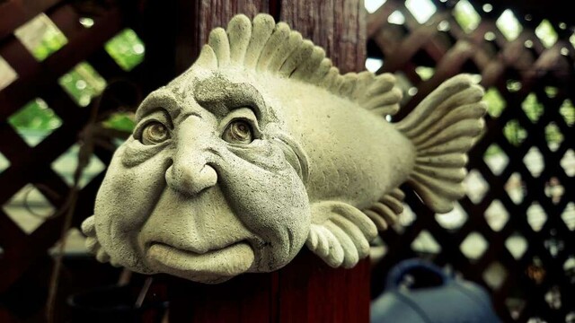 Photograph of a small concrete sculpture of a fish with a human-esque face.