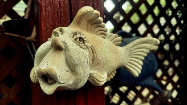 Photograph of a small concrete statue of a fish with a human-esque face.