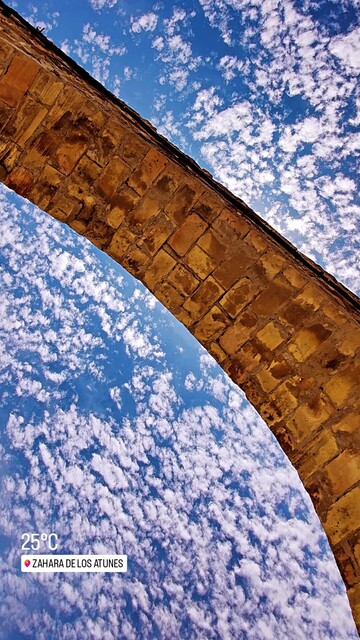 An arch of a door in a brick wall crosses the image from corner to corner, leaving on both sides an intense blue sky dotted with white clouds.