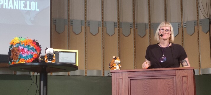 Stephanie on stage with two toy plushie hamsters that talk and a giant pom pom.