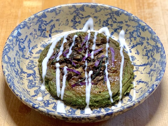 Green Okonomiyaki, adapted from “Okonomiyaki.“ Sakai, p.261. 

The objective was to make a green pancake. Kept on adding more and more dried green leaves to the batter until satisfactorily verdant. 

In a marbled blue and tan pie dish is a large green pancake that is topped with homemade Tonkatsu sauce, purple Okinawa spinach strips, Nori strips, and round maitake mushrooms. It is striped with a coconut yogurt sauce. ￼