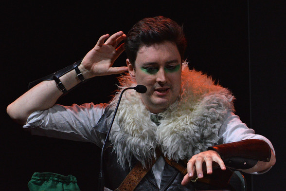 A photo of Luke Westaway as Dob the Half-Orc Bard. He has one of his arms raised and the other lowered.