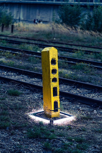 A yellow pillar between tracks on an abandoned freight yard. A square shape of LED lights was placed to highlight it. 