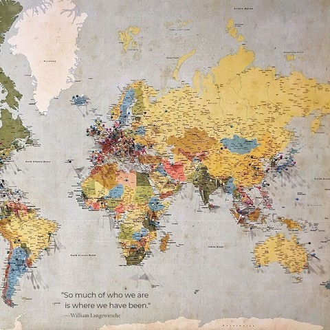 A wall map with many pins stuck in it around various countries in the world. The quote on the photo reads, “So much of who we are is where we have been.” by William Langewiesche.