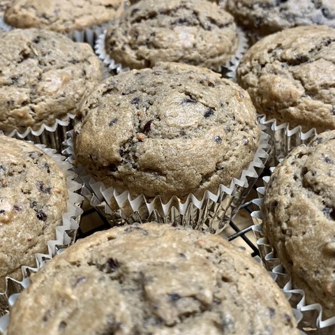A tray of light brown muffins in silver cupcake cups on a black tray on a wood countertop. 

The muffins are nicely raised and cracked at the top and bits of cranberry are visible and densely distributed. They have turned almost black. 

They were good, nicely fluffy and moist.  You could definitely and orange. 

The ingredients:
Large apple 
Equal volume cranberries
Equal volume strawberry jam
Zest of one orange, and half of the orange

1/2 cup cane sugar 
Whole block of miyoko’s unsalted butter
4 eggs

3 cups flour 
1 T baking soda 