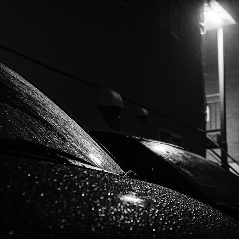 A monochromatic view of light penetrating raindrops adhered to the windshield and bonnet, creating a captivating visual play.