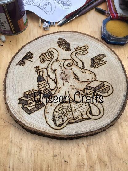 Wood slice with work in progress pyrography design of an octopus holding a lantern surrounded by books. Some books are flying.