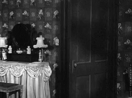 GIF of an old-fashioned bedroom, where we see a door and a vanity desk. The room is lit up by lightning, and as the light hits the mirror, a skull appears then disappears. 