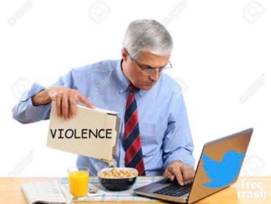 Photo of a silver haired white man with glasses, looking at his computer while having his breakfast, in the process of pouring cornflakes into a bowl. The packet he is pouring from is labelled VIOLENCE 