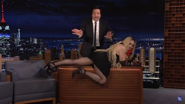 Madonna splaying herself out on Jimmy Fallon's desk, smiling to camera, with Jimmy Fallon behind her, hands out, as if to say, "God, no! Dear God, no!," though of course he really loved it