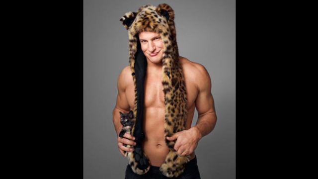 Rob Gronkowski, shirtless, smirking, leopard-print hat with streamers down the front, holding a kitten on his hip, I mean honest to God what the hell   