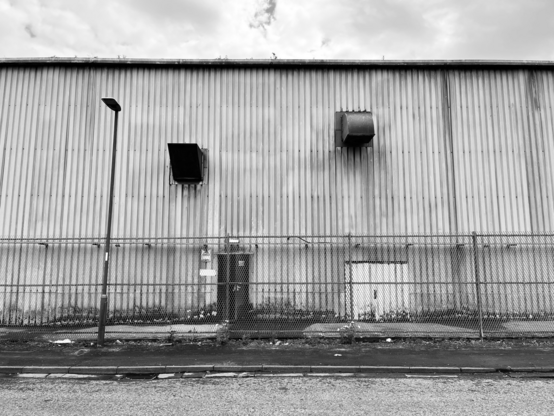 Side of a warehouse with air vents, a fence and a street light
