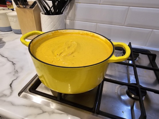 Large yellow pot full of pumpkin soup on a stove