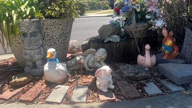 A group of front yard statuettes: tiki, goose, angel, bunny, swan, and another bunny