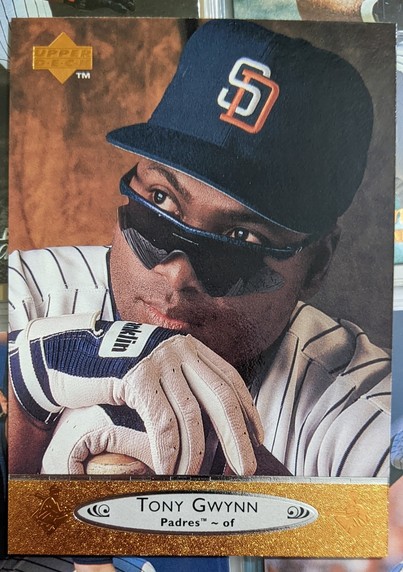 A 1996 Upper Deck baseball card depicting a close shot of Gwynn sitting with his white pinstriped jersey and blue cap with his sunglasses lowered and staring to his right side as if thinking about something while his hands are resting on a bat.knob.

Bottom of the card has a gold banner with a silver ellipse in center which shows player name, team and position.

Upper Deck had really good photography around this time.
