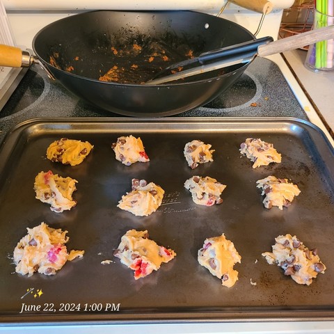 A tray of misshapen mispropotioned cookie dough with chips and cherries ready to go in the oven.