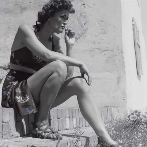 Photo of a very young Julia Child in the 1940's wearing a very short skirt and smoking a cigarette