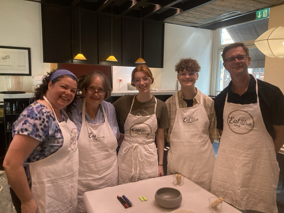 A multi-generational family wearing aprons poses together for a vacation cooking class