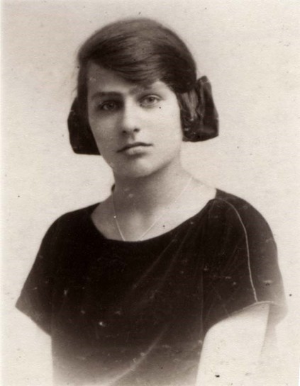 A historical black and white portrait of a young woman with chin-length hair, wearing a dark, short-sleeved blouse.