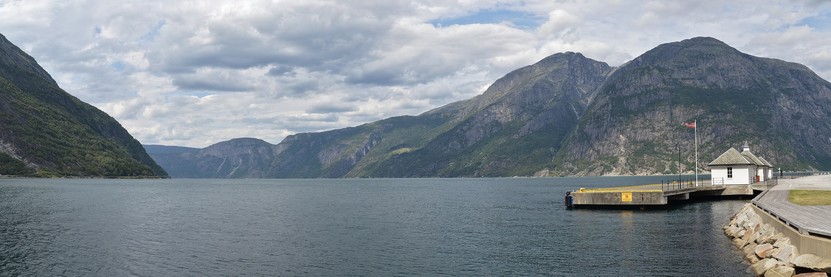 A panoramic photo of a fjord. There is a small pier on the right of the photo.
