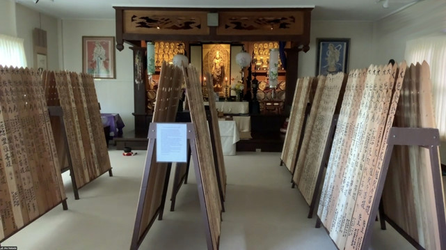 This image is a screenshot taken during today's meditation by Zoom session. A Buddhist altar in the background has more than thirty Kannon (Kuanyin) statues, but thy are blocked by many dozens of wooden slats. The slats looks something like fence posts, and are being stored here for a few days before being used in this year's bon dance. Bon dances are something like street parties to celebrate people we miss. 
