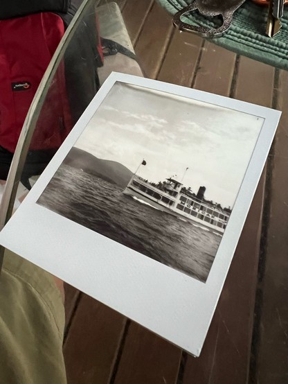 A Polaroid picture in black and white in a glass table at an angle that shows an old steamliner on a lake with the words “Mohican” on it. 