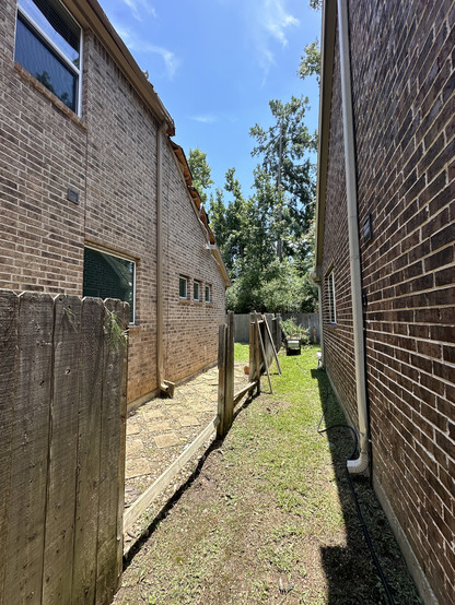 Color photo of the cleared space between two brick houses where the day before a tree fell during a hurricane. Only the partially destroyed & removed dividing fence remains. 