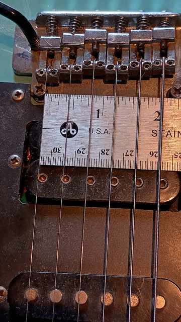 Close up of the bridge of a Dean Z Playmate 80s plywood superstrat (they were about $150 on reverb last I checked) showing the 2 point bridge and saddles and part of the bridge humbucker, with a ruler showing the string span is two inches, which is narrower than a standard fender guitar bridge.
This is because they didn't make humbuckers in the 80s with fender string spacing. It's the spacing of a Gibson neck pickup.
Bridges and bridge pickups this narrow are hard to find.