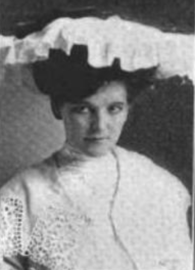 Nena Blake, a light-skinned young woman with dark hair in an updo, wearing a ruffled wide white hat and a white lace jacket