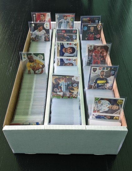 A 3000ct box of sleeved soccer cards on a dark chocolate dinner table, the first base card of each set is pulled up for reference