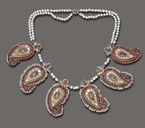 An antique Persian multi-gem and pearl bead necklace, approx 40cm long.
Composed of a series of six vari-cut ruby and diamond paisley plaques, each centering upon a foil-backed pear-shaped emerald or simulated emerald accent, enhanced by cabochon emerald and seed pearl trim, joined by pearl bead spacers, to the two-strand pearl bead backchain, and clasp of similar design, mounted in gold, mid-late 19thC. Sold at auction by Christies, October 2004