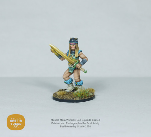 wargame model. Warrior woman. Dirty blonde wearing a sleevless top in mint green with light blue fur at the shoulders and tops of her white boots. She holds a glowing yellow sword with green hilt. White background.