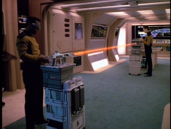 Geordi and Data run tests on a Phaser Rifle in Engineering.

