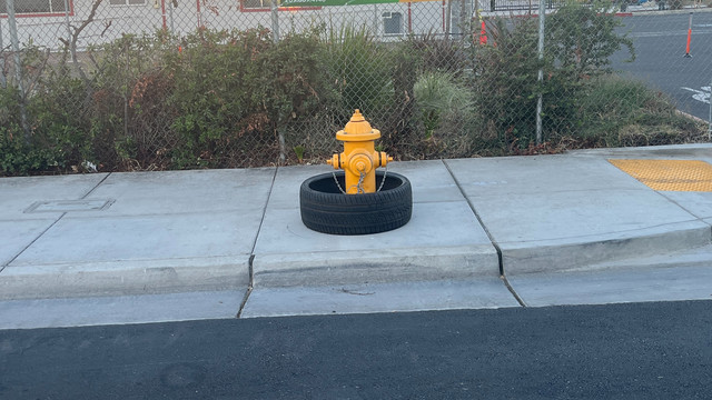 A yellow fire hydrant around which sits a tire, in the middle of a sidewalk