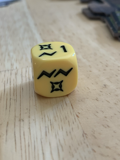 A yellow die used in a table top star wars game that looks like a pained face
