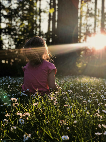 Photo of little girl sitting in a field feeling the sun on her face, by Melissa Askew on Unsplash.