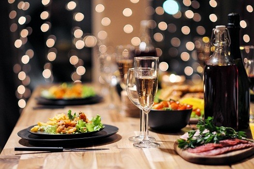 A wooden table laid out for dinner, with black plates of food, wine and water glasses, and blurred fairy lights in the background.