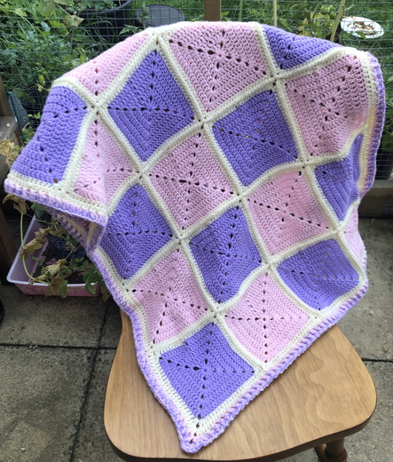 Crochet blanket made of pink and lilac squares with cream border.