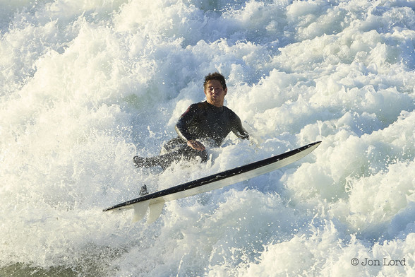 A Colour Photo In Landscape Format. In The Centre Of The Image Is A Male Surfer Facing Towards The Camera. He Has Just Been Knocked Off His Surf Board And Is Surrounded On All Sides By Breaking Surf. His Board Is Airborne And Slightly Ahead Of The Surfer. Our Man Has Short Dark Hair, Has An Expression As If He Is Holding His Breath And Is Wearing A Black Wetsuit. Shot Taken Early In The Morning At Hermosa Beach, California. 2014