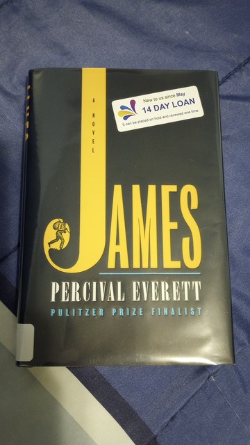 The cover of a hardback book. It contains the title of the book James: A Novel and the author, Percival. The colors of the cover and lettering are black, yellow, white, and blue.