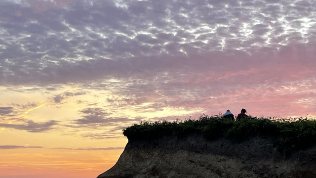 Two people watch the sunset from a rocky outcrop in Widemouth Bay