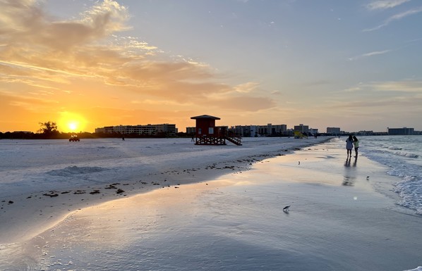 Sunset orange glow with clouds over wide beach with red lifeguard shack and couple walking along surf 