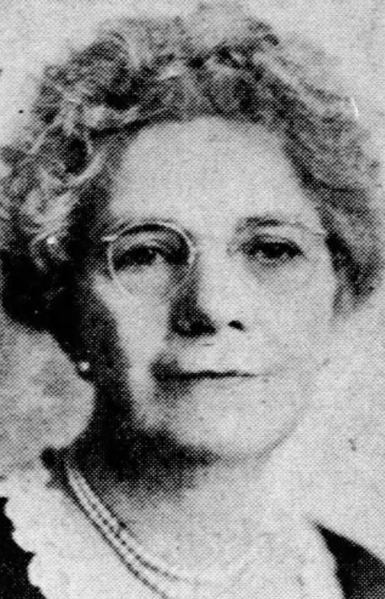 Mabel Washbourne Anderson, from a 1949 newspaper; an older woman with grey curls and olive skin, wearing glasses and pearls and a dark top with a white lace neckline detail
