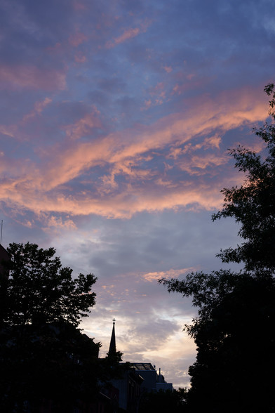 turbulent skies of light blue and orange over silhouetted trees and buildings