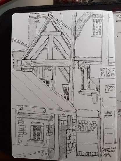 Photo of a pencil and inkpen drawing of old wooden timbered buildings with small multi-paned glass windows, chimneys and the awning of a market stall in front plus the edge of a Kreperie on the right. Back of The Shambles, York, UK