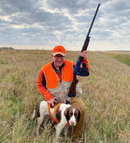 Tim Walz, newly-picked running mate of Kamala Harris, crouches in a wide-open field, holding a rifle in one hand, the other hand steadying his brown-and -white hunting dog’s flank. 