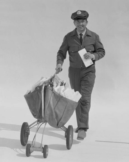 Stock photo of a smiling 1950s mailman pushing a three-wheeled satchel cart full of mail