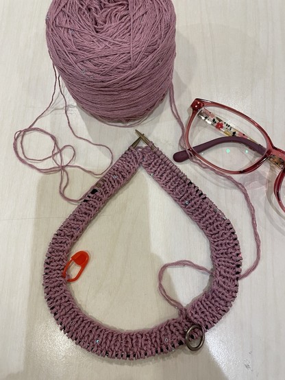 A beginning knit project on the needles using pink yarn with sparkles, my pink eyeglasses lying close by