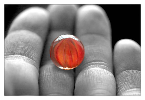 An orange marble resting on a man's fingers.