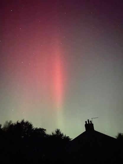 The night sky is lit with a greenish glow that highlights a vivid streak of red aurora 